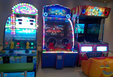 A row of brightly lit arcade game machines including Graveyard Smash and Fire Man in an indoor family entertainment center.