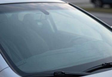 Macro photography of a new, pristine car windshield showing a subtle manufacturer's stamp of quality, reflecting a soft light blue sky.