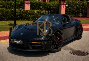 Sleek black Porsche 911 Targa convertible for rent in Marbella, parked on a sunny street in front of a luxury resort.