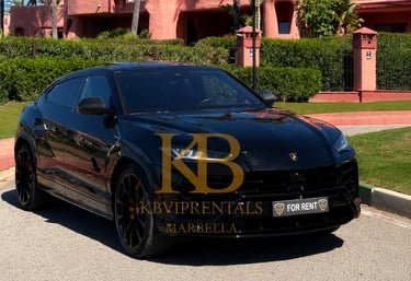 Black Lamborghini Urus luxury SUV rental parked in Marbella near a pink Mediterranean villa.