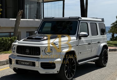 White Brabus G-Wagon luxury SUV rental parked on a sunny road in Marbella with sea views.