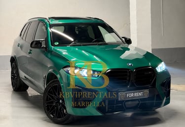 A metallic emerald green BMW X5 M luxury SUV with black rims parked in a garage for rent in Marbella.