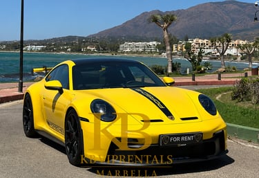 Yellow Porsche 911 GT3 luxury car rental parked on the Marbella coast with mountain views.