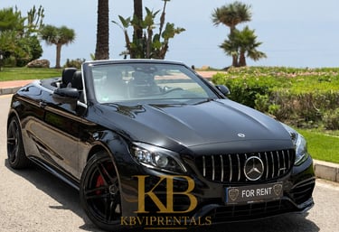 Black Mercedes AMG convertible luxury car rental parked in Marbella near tropical palm trees.
