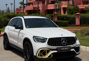 White Mercedes-Benz AMG SUV for rent parked in front of a luxury pink Mediterranean villa in Marbella.