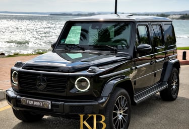 Black Mercedes G-Wagon luxury car rental parked by the sea in Marbella, Spain.