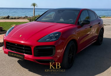Red Porsche Cayenne Coupe luxury car rental parked by the ocean in Marbella.
