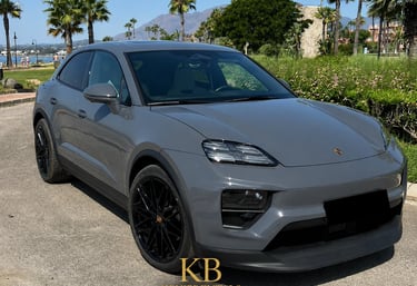 Luxury grey Porsche Macan electric SUV parked in Marbella with palm trees and mountains.