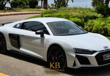White Audi R8 V10 luxury car rental parked on a sunny road near the coast in Marbella.