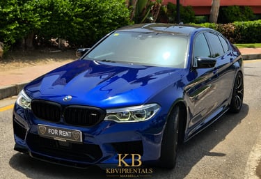 Luxury blue BMW M5 sedan for rent parked on a sunny street in Marbella, Spain.