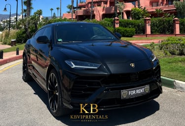 Black Lamborghini Urus luxury SUV for rent in Marbella parked near a tropical resort.