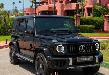 Black Mercedes-Benz G-Class AMG luxury SUV for rent parked in front of a Mediterranean resort.
