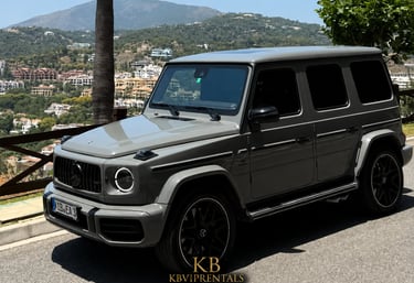 A luxury grey Mercedes-Benz G-Wagon parked on a scenic Marbella hillside overlooking the mountains.