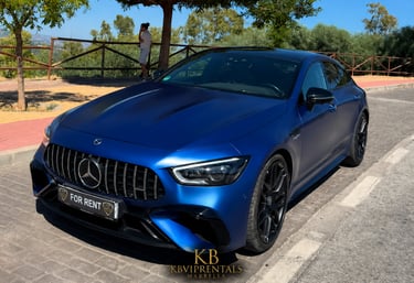 Matte blue Mercedes-AMG GT 63 S 4-Door Coupe luxury car rental parked on a sunny street in Marbella.