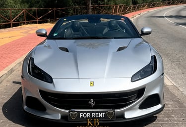 Silver Ferrari Portofino luxury convertible car for rent parked on a sunny street in Marbella.