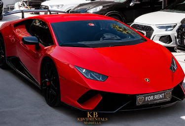 Red Lamborghini Huracan luxury car for rent parked among exotic sports cars in Marbella.