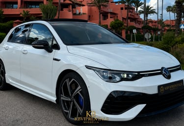 White Volkswagen Golf R luxury rental car parked in front of a Mediterranean resort in Marbella.