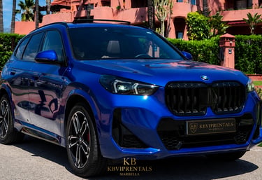 Blue BMW SUV rental car parked at a luxury resort in Marbella with KB VIP Rentals logo.