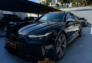 Black Audi RS7 luxury car rental parked in a Marbella showroom with LED headlights on.