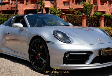 Silver Porsche 911 Targa luxury rental car parked in front of a Mediterranean resort in Marbella.