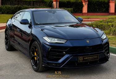 Luxury dark blue Lamborghini Urus SUV parked on a paved road for luxury car rental.