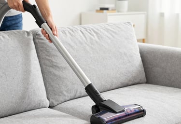 a woman in a green shirt and black gloves vacuuming a gray ottoman