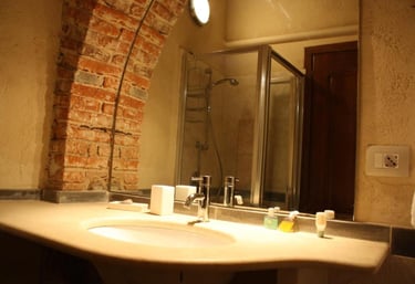 Rustic bathroom featuring a stone sink vanity and exposed red brick archway with a glass shower.
