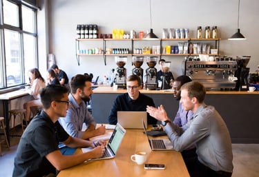 Diverse team of professionals having a business meeting with laptops in a modern cafe.