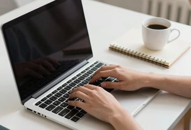 A high-quality photo of hands typing on a laptop on a clean white desk, next to a notebook and a cup of coffee, in a bright North American home office setting.