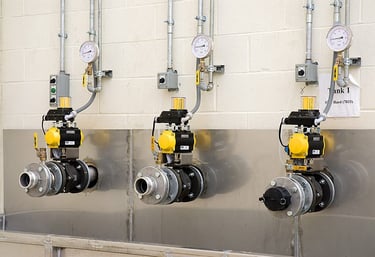 Three industrial ball valves with pneumatic actuators and pressure gauges mounted on a wall.