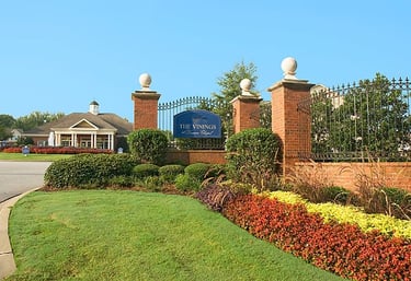 Brick entrance sign for The Vinings at Duncan Chapel apartment complex with manicured landscaping and a black iron fence.