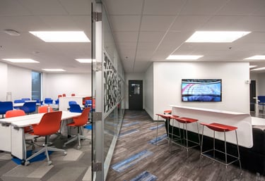 Modern office collaboration space with colorful seating, glass partitions, and a wall-mounted TV.