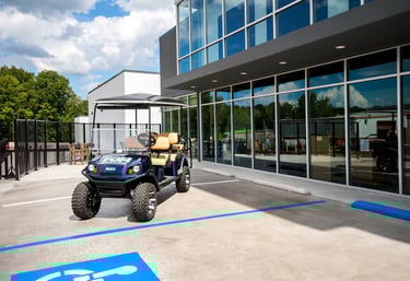Custom blue lifted golf cart parked in a modern dealership lot with large glass windows.
