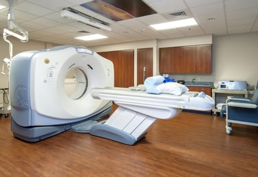 A modern GE medical CT scanner in a sterile hospital diagnostic imaging room with an adjustable patient table.