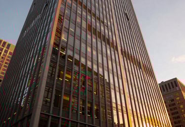 A modern, wide-angle view of a high-rise office window in a North American / US city at sunset, with warm orange light hitting the glass.