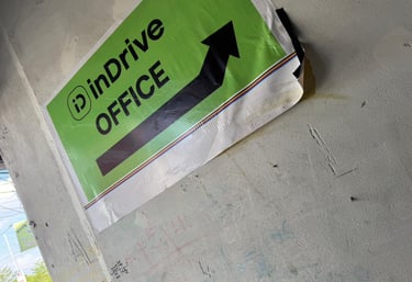Green and white inDrive OFFICE directional sign with a black arrow on a grey concrete wall.