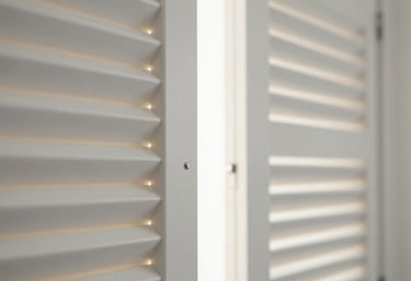 Detail of high-quality white plantation shutters partially open, letting in shards of warm light. Modern, clean aesthetic focusing on the hardware and material quality.