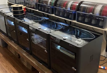 A row of Bambu Lab 3D printers with AMS filament management systems in a professional workshop.