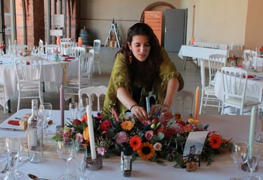 Estelle, créatrice de l’Ensorce’Fleurs, décore une table de mariage avec un bouquet coloré.