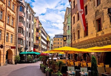 Colorful historic buildings and outdoor cafe tables with yellow umbrellas in Innsbruck Old Town, Austria.