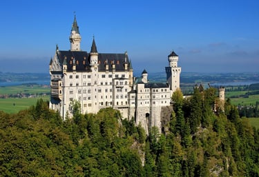 The Neuschwanstein Castle in Bavaria, Germany, stands on a rugged hill above a lush green forest.
