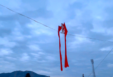 Moment poetique, un funambule traverse une ligne drapé dans un grand tissu rouge