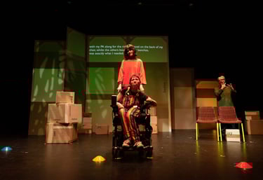 A white electric wheelchair user in front of a white person in orange. A BSL interpreter to the side