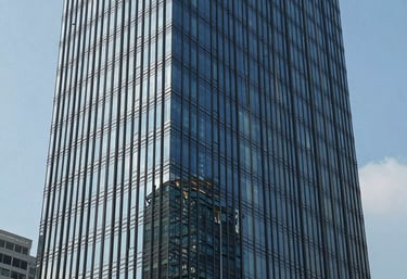 An architectural shot of a modern corporate headquarters in Jakarta's central business district during a clear day. The building's glass facade reflects the professional and transparent nature of the business.