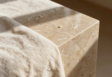 Close-up detail photography of natural textures in a luxury spa studio in Valencia, smooth champagne limestone, warm ivory linen fabric, polished wood, soft natural sunlight casting gentle shadows.