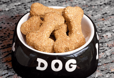 Crunchy bone-shaped homemade dog treats piled in a black ceramic bowl on a granite countertop.