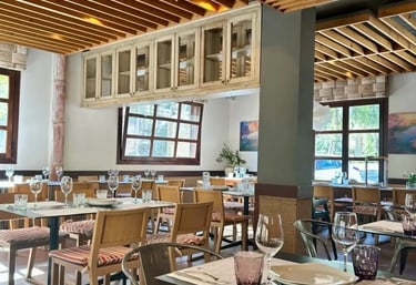 Interior del Restaurante con las mesas preparadas y un ambiente cálido de madera y luz natural.