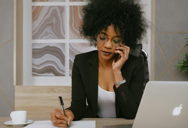 Une femme en tailleur noir au téléphone qui prend des notes sur une feuille