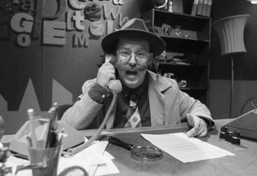 Vintažinio stiliaus detektyvas su fedora kalbasi rotaciniu telefonu prie stalo su rašomąja mašinėle.