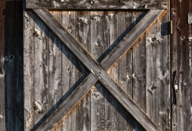 A rustic barn door detail in a Northern European / North American farm setting, with weathered wood and soft afternoon shadows.